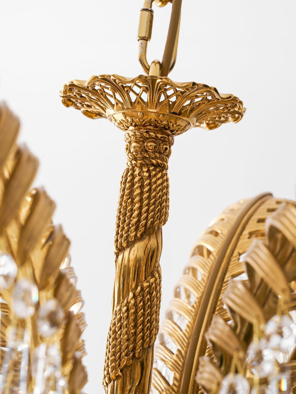 Close view of the pierced brass top cap and rope-twist stem of this Clérachic chandelier, on a white backdrop.