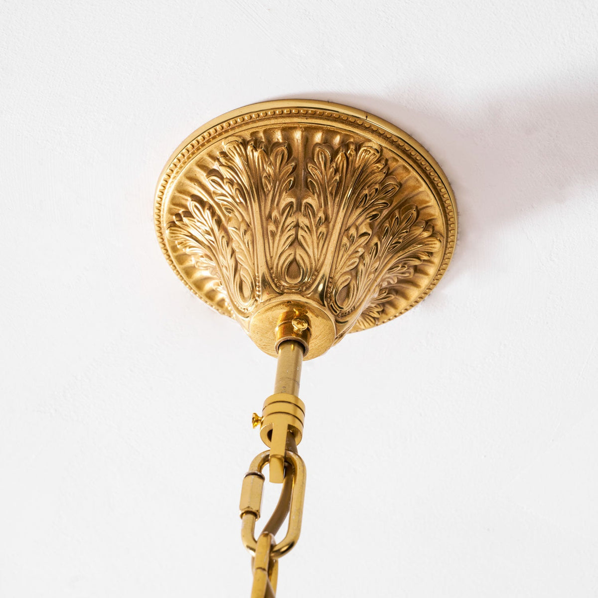 Underside of the carved brass ceiling plate that holds this Clérachic chandelier on its gold chain.