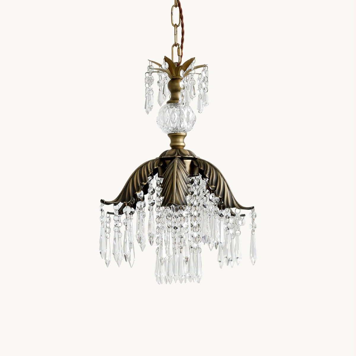 Clérachic pendant with a bronze palm-leaf canopy and clear crystal drops, hung on a chain against a plain white backdrop.