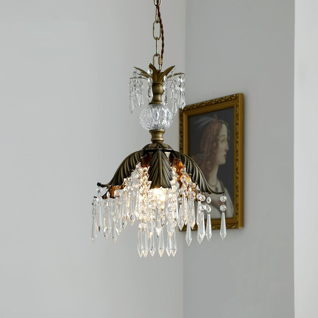 A lit Clérachic pendant with a leaf-shaped bronze shade and crystal drops hangs beside a gilt-framed portrait on a white wall.