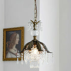 Clérachic crystal pendant with a bronze leaf canopy glows beside a gilt-framed portrait, with a glass finial above the shade.