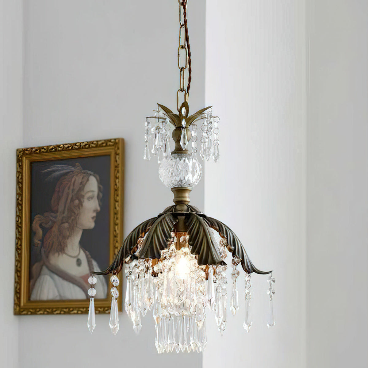 Clérachic crystal pendant with a bronze leaf canopy glows beside a gilt-framed portrait, with a glass finial above the shade.