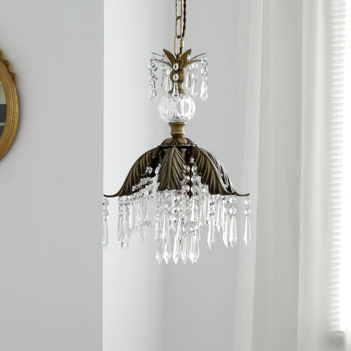 Clérachic pendant with a bronze palm-leaf shade and long crystal drops hangs unlit in front of a sheer curtain.