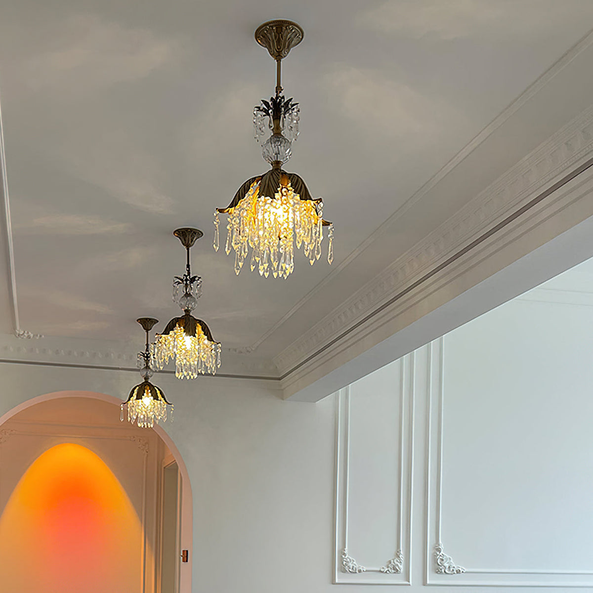 Three Clérachic crystal pendants of descending height glow warm below a cornice, with an arched doorway beyond.