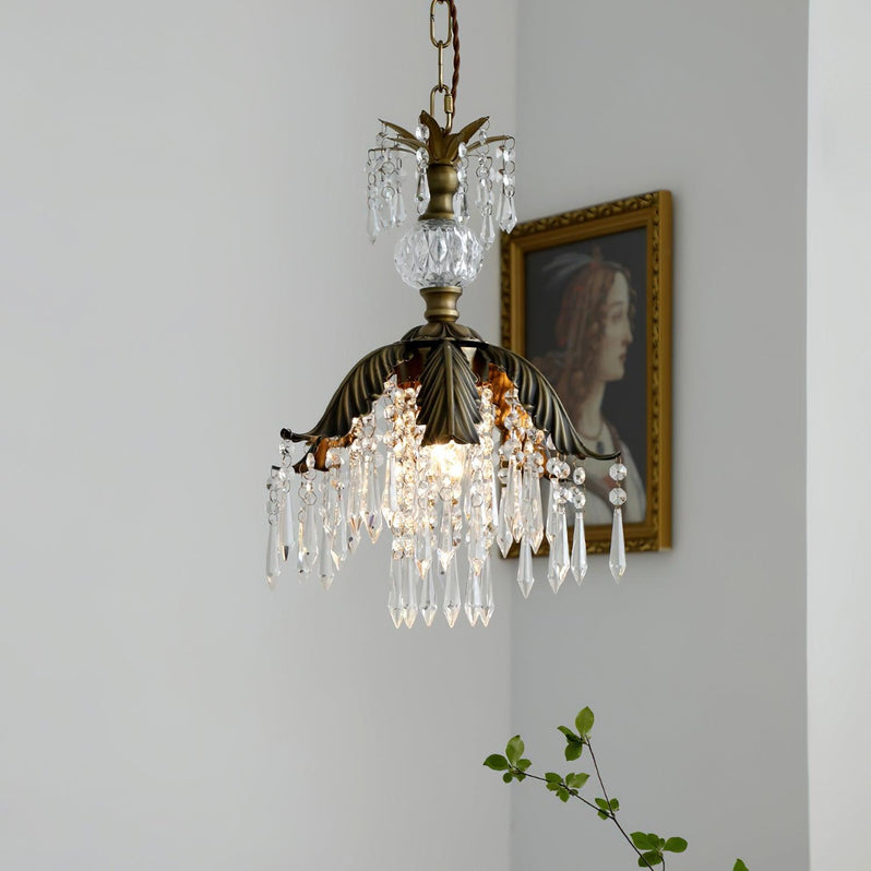 A lit Clérachic pendant with a bronze leaf shade and crystal drops hangs near a gilt-framed portrait and a green stem.