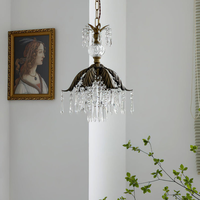 A Clérachic crystal pendant with a bronze leaf shade hangs on a chain beside a portrait, with green stems below.