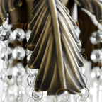Close view of a bronze palm leaf on this Clérachic pendant, with linked crystal beads hanging around it.
