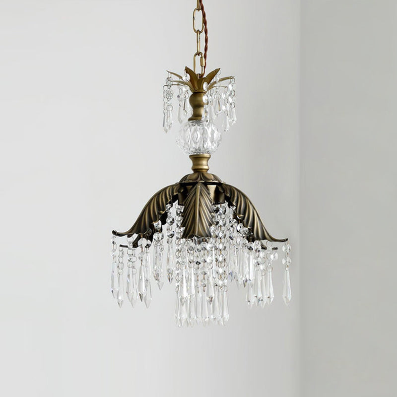 Clérachic pendant with a chain, glass finial, bronze palm-leaf shade and crystal fringe, hung against a pale grey wall.