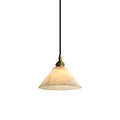 The Clérachic Xen pendant hangs on a plain white backdrop, showing its cone alabaster shade and knurled brass fitting.