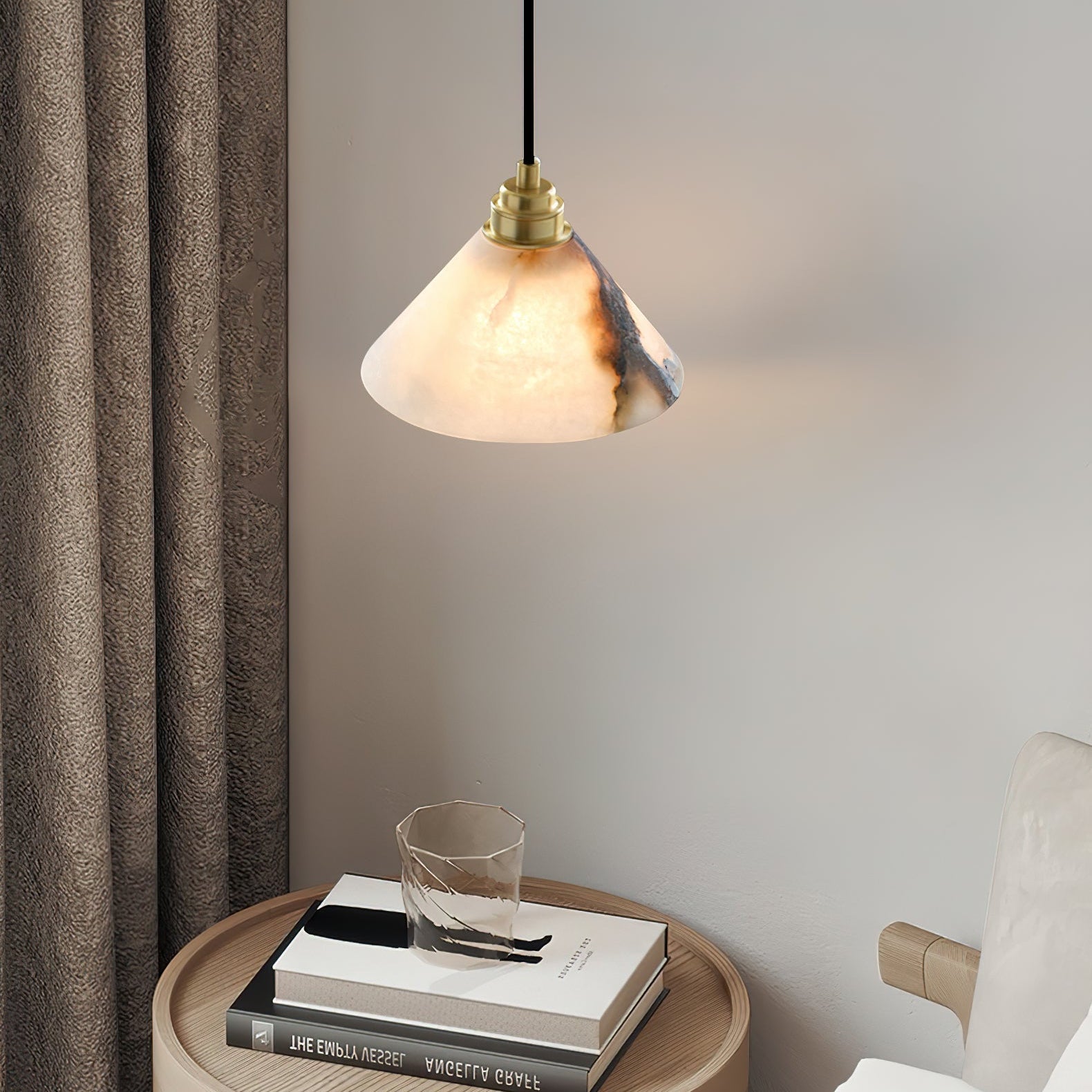 A Clérachic Xen alabaster pendant lights a bedside table styled with linen curtains, stacked books, and a faceted glass.
