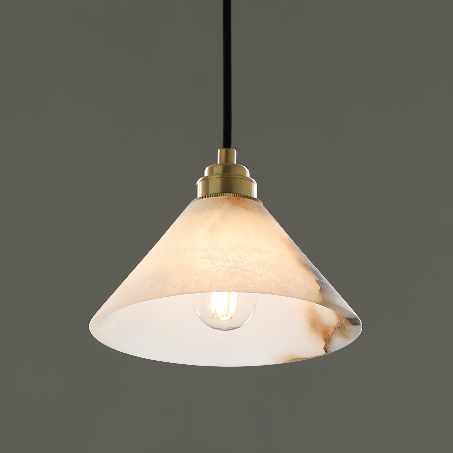 Close on the Clérachic Xen pendant's lit shade, the warm filament bulb glowing through veined natural alabaster.