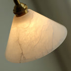 Angled close-up of the Clérachic Xen pendant near its brass collar, revealing the alabaster's natural fissures and tone shifts.