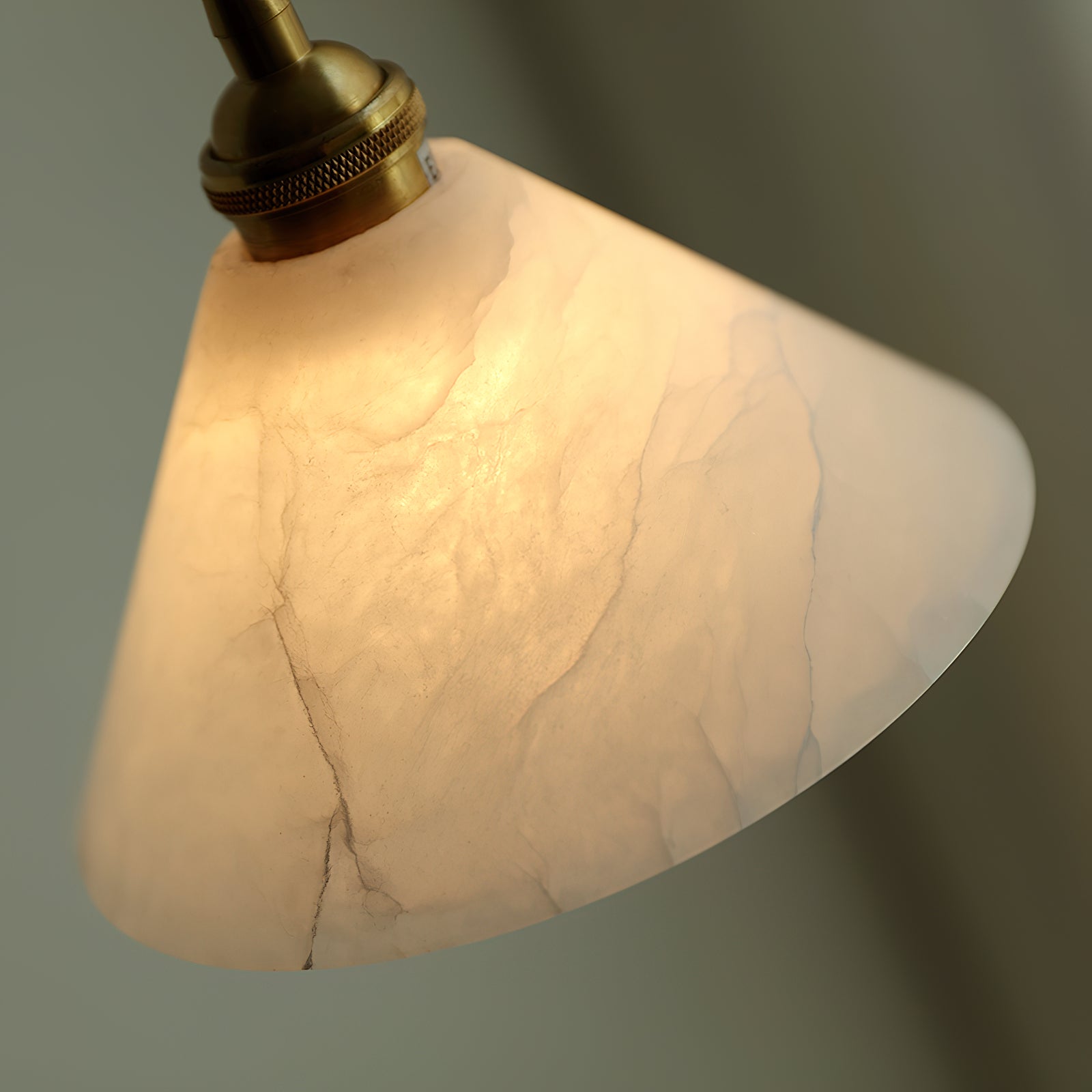 Angled close-up of the Clérachic Xen pendant near its brass collar, revealing the alabaster's natural fissures and tone shifts.