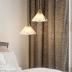 Two Clérachic Xen pendants hang beside a woven brown curtain, warming a bedroom corner near the headboard.