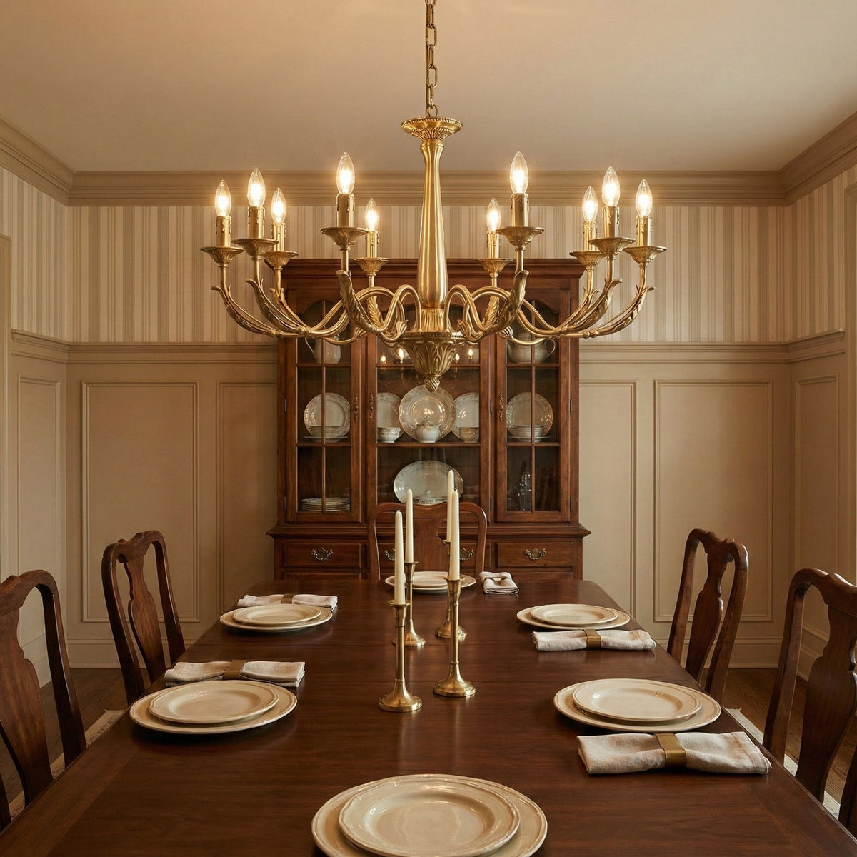 A brass candle-style Clérachic chandelier above a long wooden dining table laid with plates, in a panelled dining room.