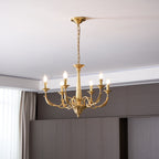 A brass Clérachic chandelier with six lit candle-style bulbs, hung from a chain below a recessed ceiling edge.