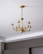 Hung from a ceiling canopy and chain above a dark panelled wall, this brass candle-style Clérachic chandelier is unlit.