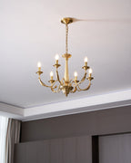 Lit and hung from a chain in a grey room with panelled walls, this brass Clérachic chandelier has six candle-style arms.