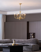 High above a grey sofa and a dark coffee table, a small brass candle-style Clérachic chandelier is lit.
