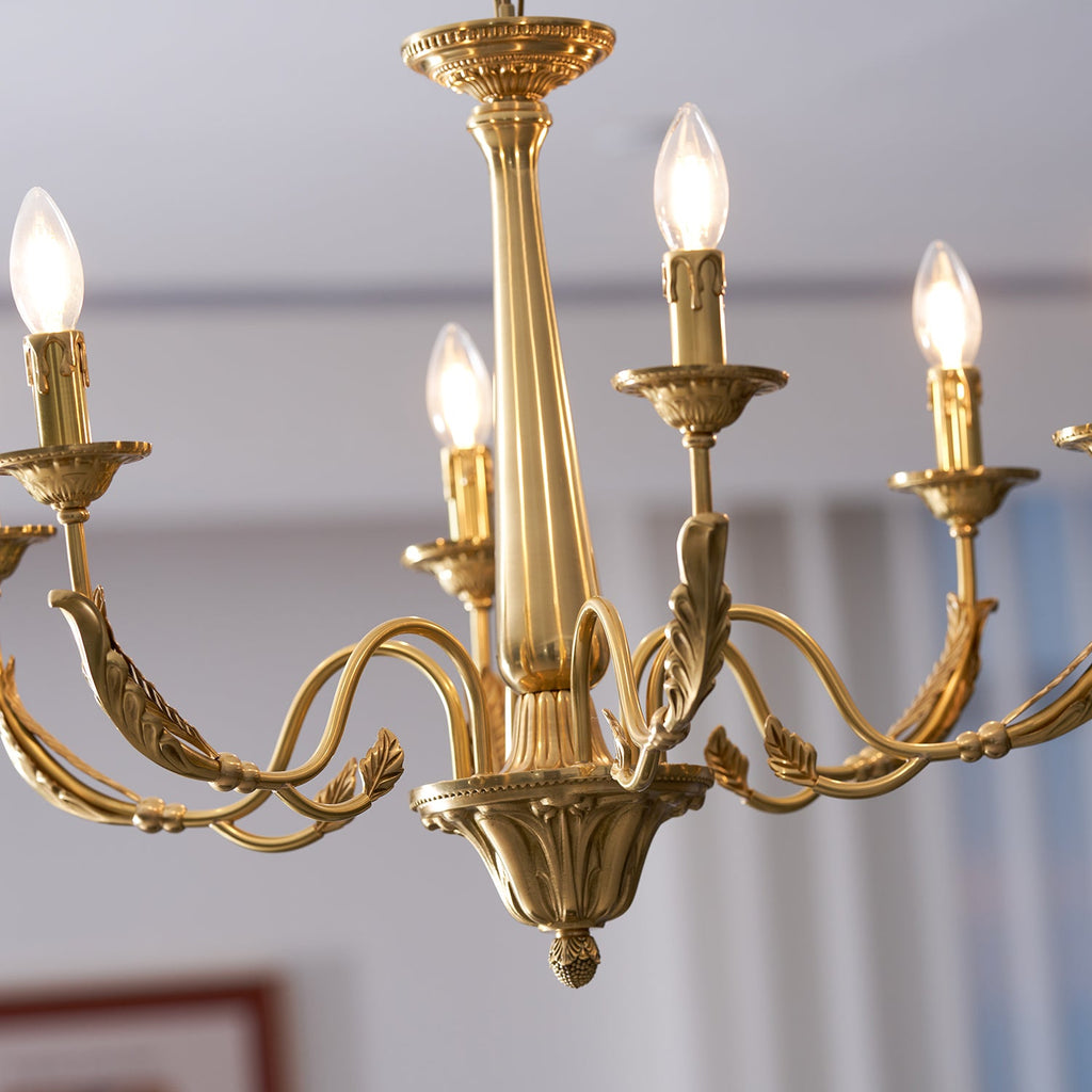 Close view of the brass arms, leaf details and candle sleeves of this Clérachic chandelier, with the bulbs glowing.
