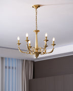 A brass candle-style Clérachic chandelier with six lit bulbs, hung from a long chain beside a curtain and a dark wall.