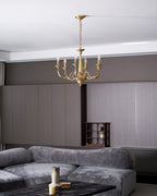A brass candle-style Clérachic chandelier lit high in a living room with a grey sofa, a dark table and a wine rack.