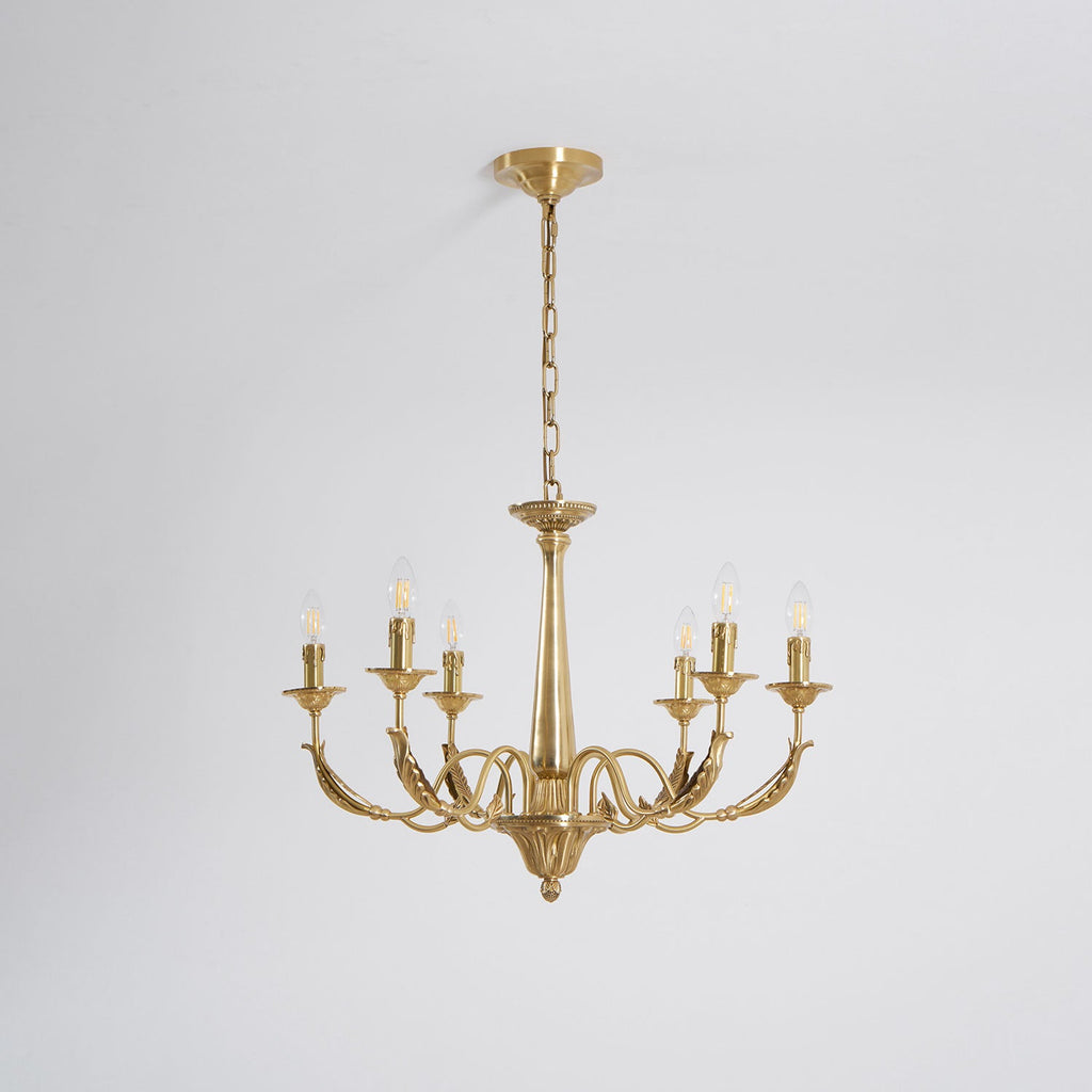 On a plain pale grey backdrop, this brass candle-style Clérachic chandelier is lit, with six arms.
