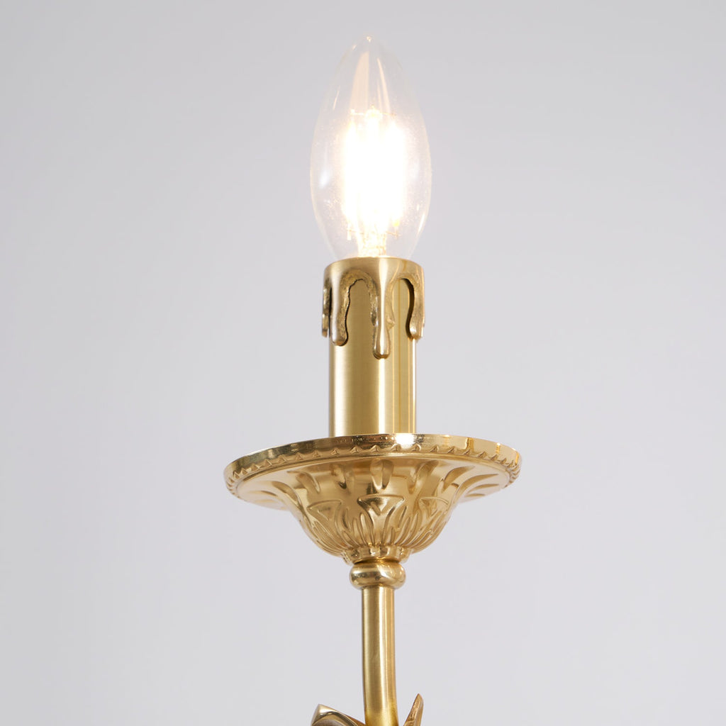 Close view of one candle-style bulb on this brass Clérachic chandelier, with a ribbed sleeve and a leaf-patterned drip tray.