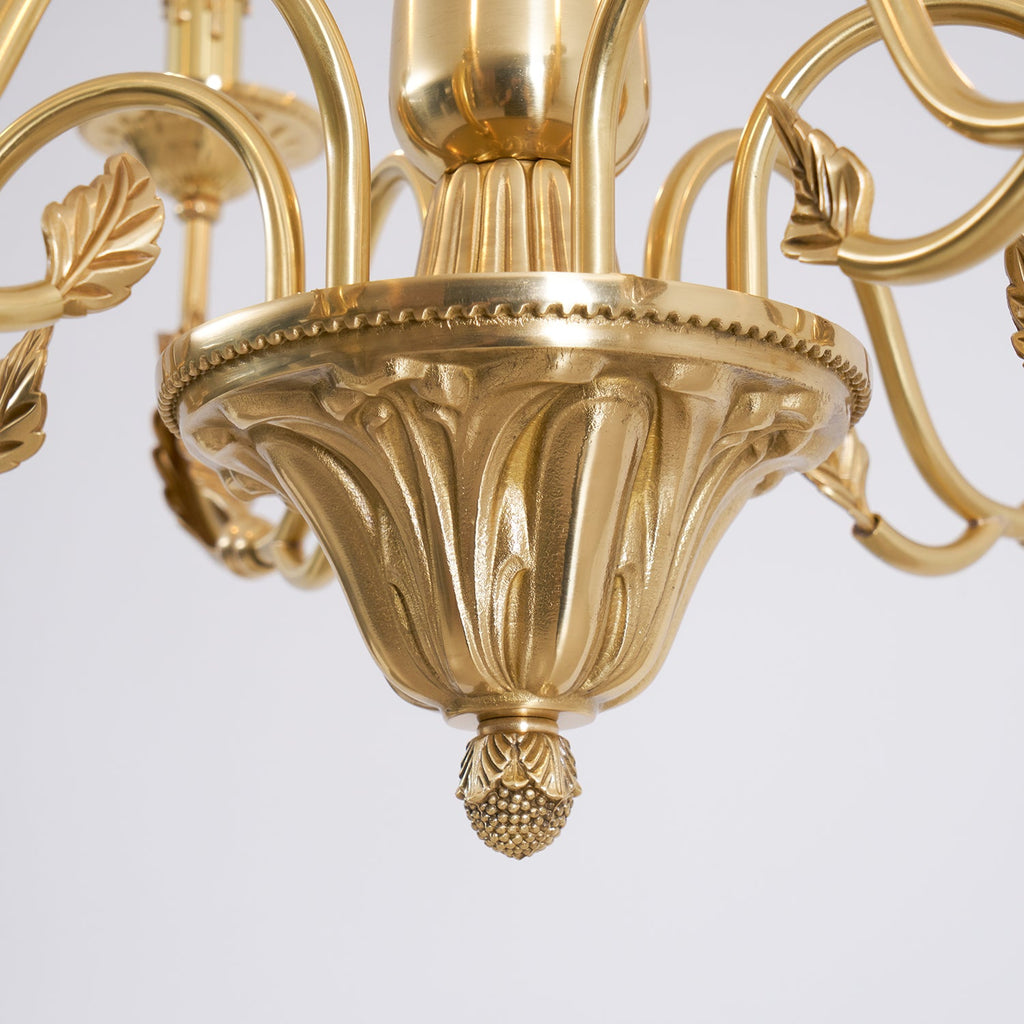 Close view of the fluted brass bowl, leaf details and acorn-shaped finial at the base of this Clérachic chandelier.