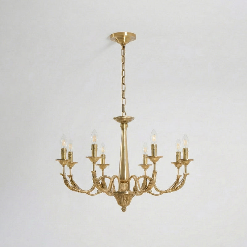 A larger brass candle-style Clérachic chandelier with eight arms, lit, hung from a chain on a pale backdrop.