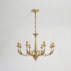 A larger brass candle-style Clérachic chandelier with eight arms, lit, hung from a chain on a pale backdrop.