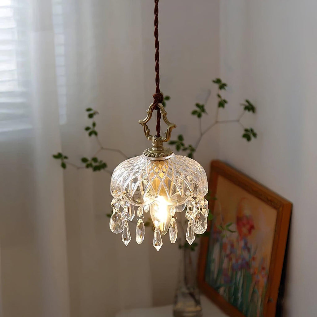 Clérachic cut-glass pendant lit beside a sheer curtain, with a bare green twig and a framed floral painting leaning on a table behind it.