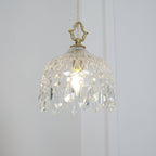 Clérachic crystal-drop pendant lit on a white wall, with a brass crown-shaped finial and a diamond-patterned glass bowl.