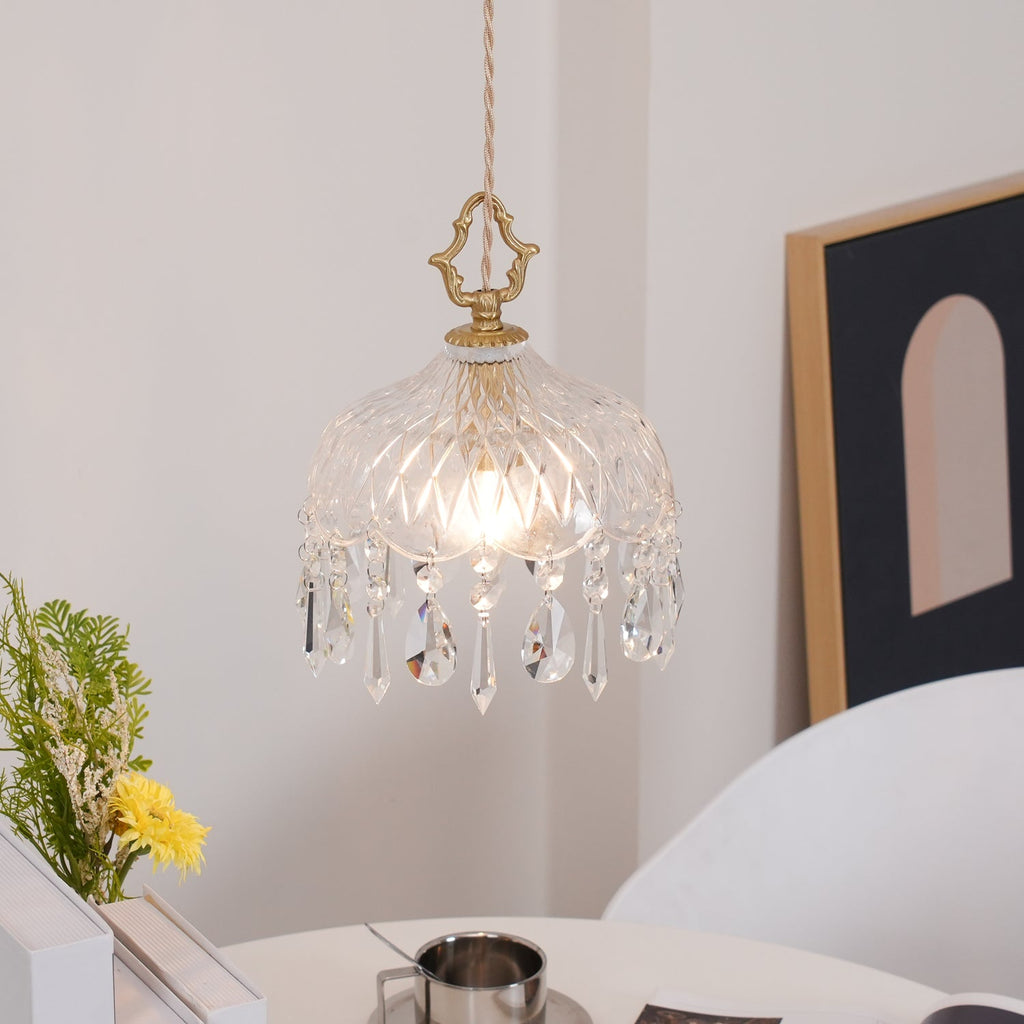 Clérachic glass pendant lit above a white table, with a yellow flower in a vase, a framed arch print and a steel cup nearby.