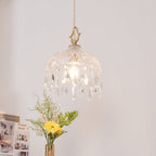 Clérachic faceted glass pendant lit against a blush wall, with a yellow flower and sprigs of greenery in a vase below.