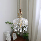 Clérachic cut-glass pendant with large crystal teardrops, lit beside a white curtain, a cherub figure and a framed mirror below.