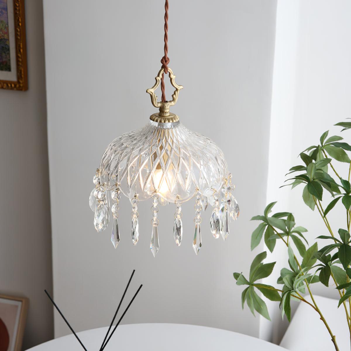Clérachic crystal-drop pendant lit in a bright room, with a twisted brown cord and a leafy green plant at the right.