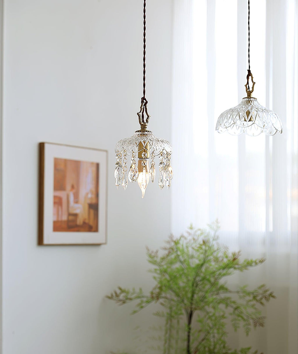 Two glass pendants in a bright room, with a Clérachic crystal-drop pendant at the front and a second shade hung beyond it, near a framed print.