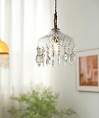 Clérachic crystal-drop pendant lit in front of sheer curtains, with an amber glass shade to the left and a framed print on the wall.