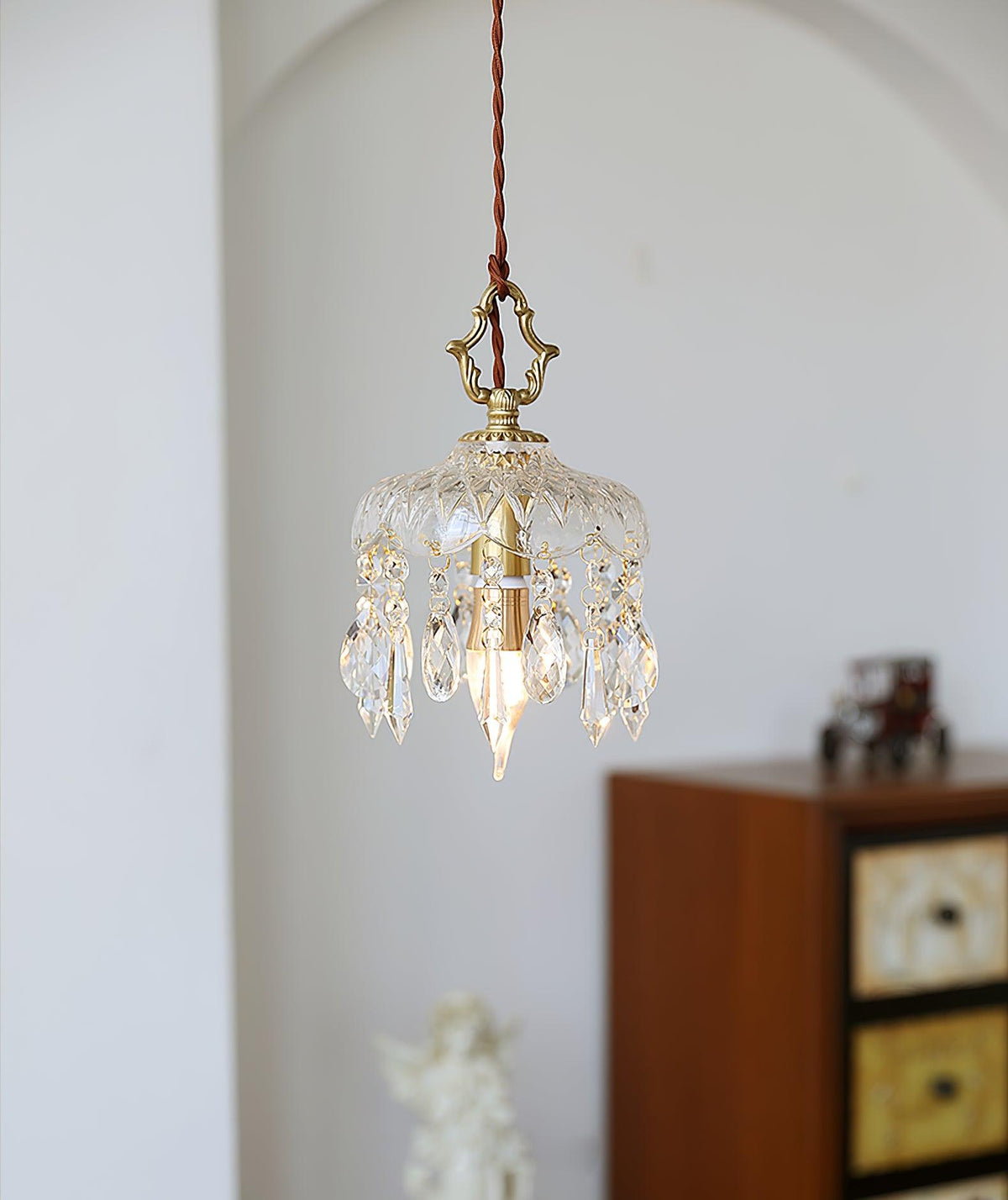 Clérachic crystal-drop pendant lit in a white arched alcove, with a wooden cabinet and a small ornament in the background.