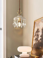 Clérachic crystal-drop pendant lit beside a gilt-framed landscape painting and a white mushroom-shaped lamp, in a room corner.