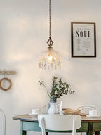 Clérachic crystal-drop pendant lit above a green-painted dining table with a vase of greenery, a white chair and a framed print on the wall.