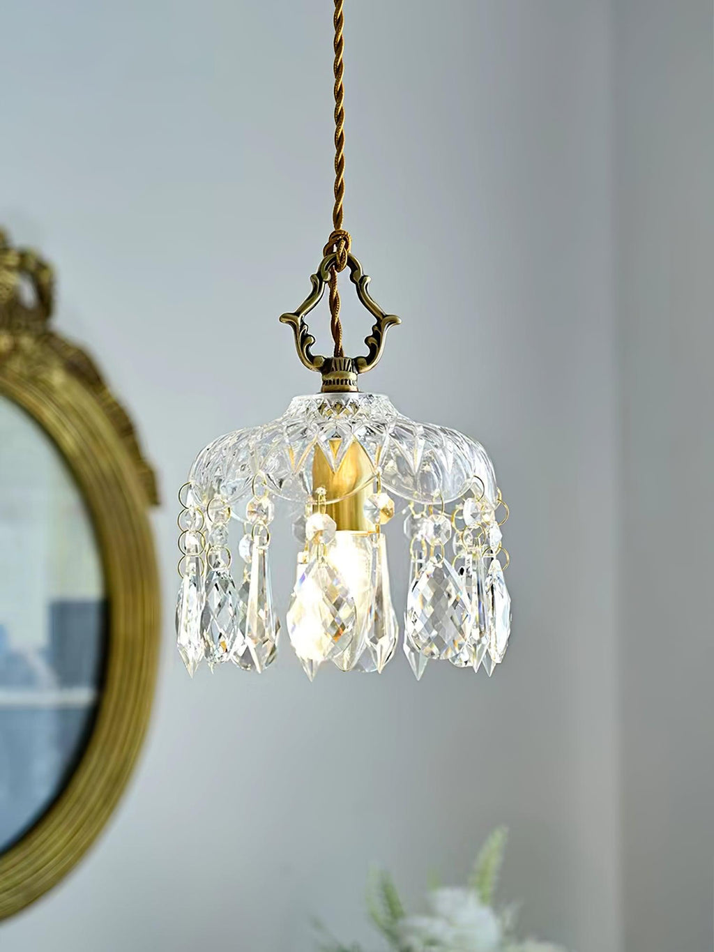 Clérachic crystal-drop pendant lit in front of a gilt-framed round mirror, with a pale blue wall and a brass-coloured finial above.