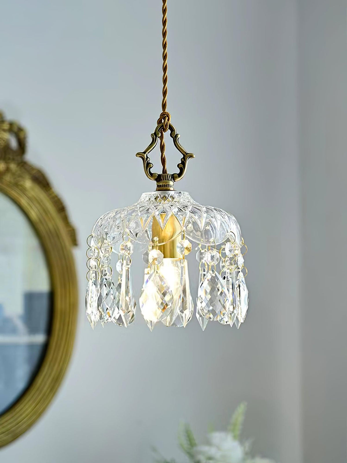 Clérachic crystal-drop pendant lit in front of a gilt-framed round mirror, with a pale blue wall and a brass-coloured finial above.