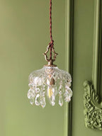 Clérachic crystal-drop pendant lit against a sage green panelled wall with an ornate carved moulding at the right.