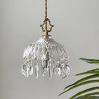 Clérachic crystal-drop pendant on a pale grey backdrop, with a diamond-cut glass bowl and a palm leaf at the right edge.