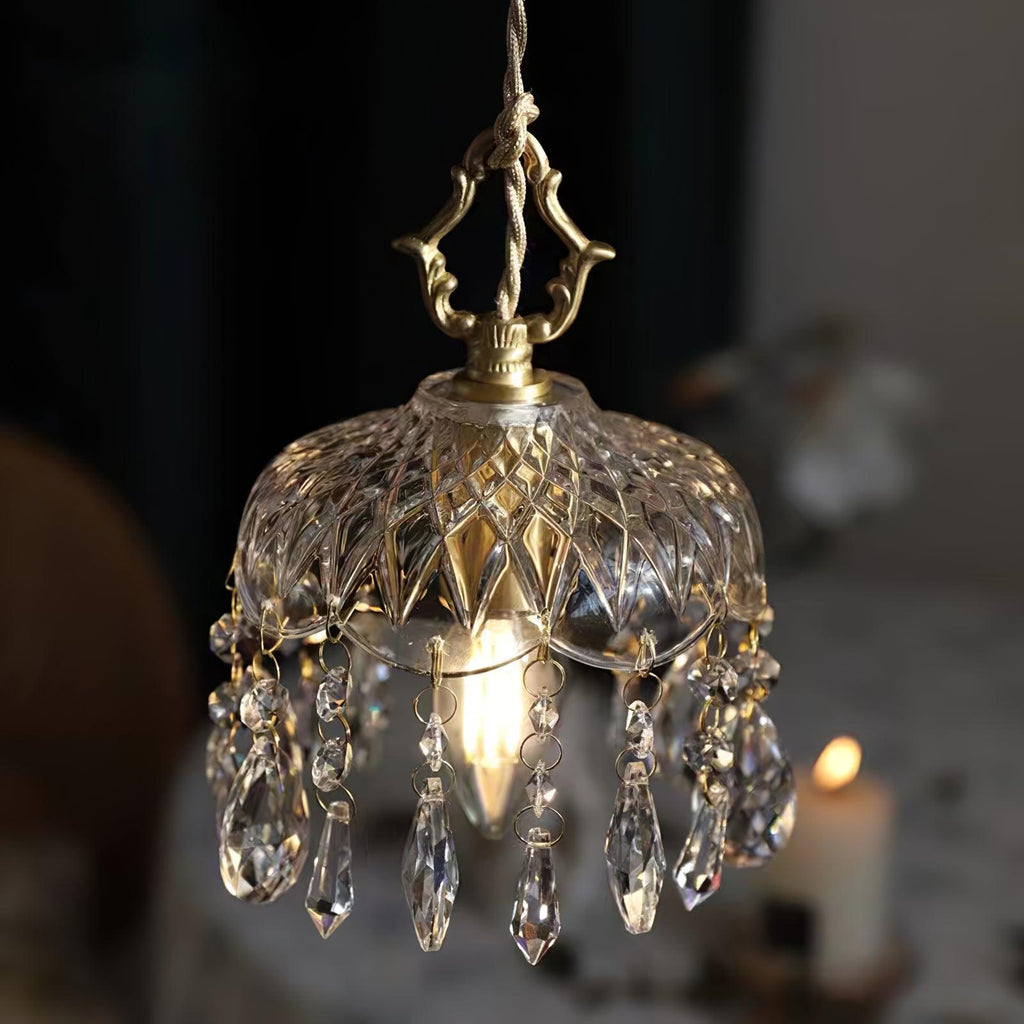 Clérachic crystal-drop pendant glowing on a dark backdrop, with a candle blurred behind and a brass finial above a smoke-tinted glass bowl.