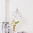 Clérachic crystal-drop pendant with a dark brass top, lit above a white table with a gold-framed vase of yellow flowers and books.