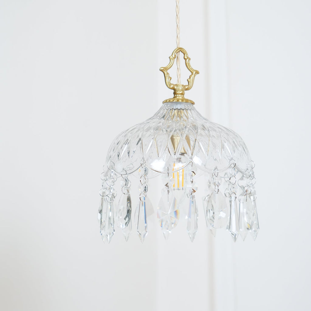 Clérachic crystal-drop pendant lit softly against a white wall, with pale cord, a diamond-cut bowl and long crystal drops.