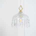 Clérachic crystal-drop pendant lit softly against a white wall, with pale cord, a diamond-cut bowl and long crystal drops.